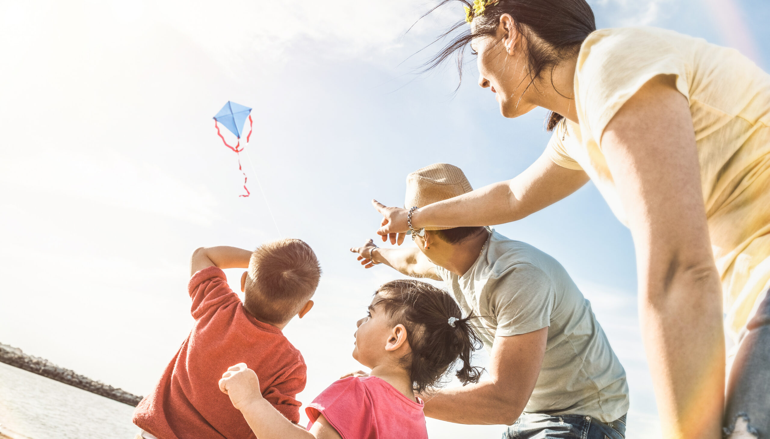 Happy family with parents and children playing together with kite at beach vacation - Summer joy happiness concept with mixed race people having candid genuine fun - Warm vintage backlight filter