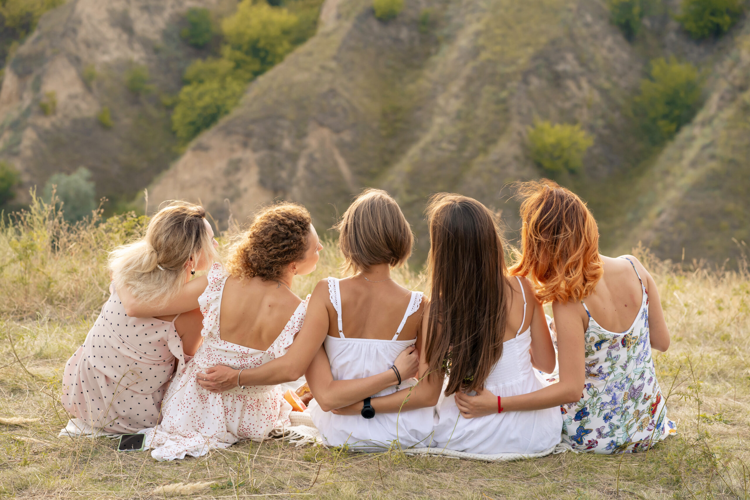 Shoot from back. The company of female friends having fun, hugs each other and enjoy hills landscape.