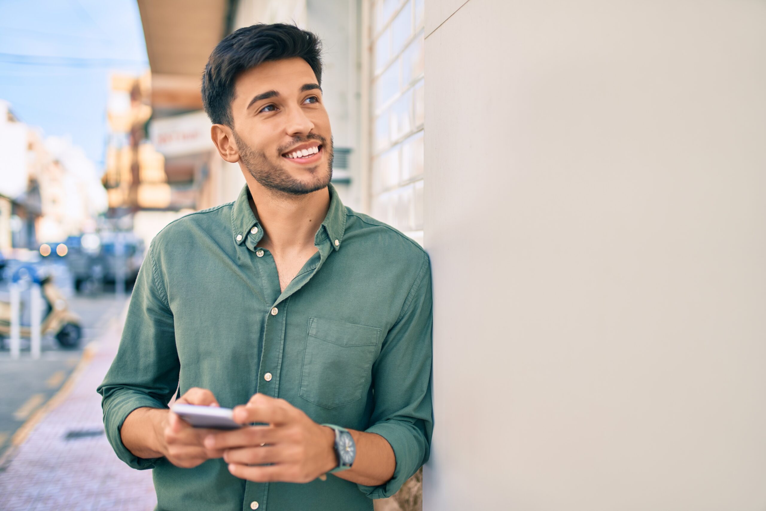 Young latin man smiling happy using smartphone at the city.